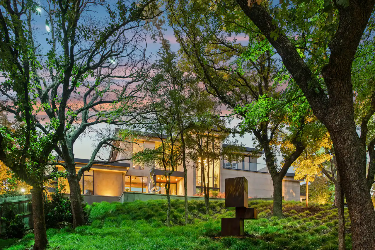 Casa contemporânea iluminada entre árvores ao entardecer.