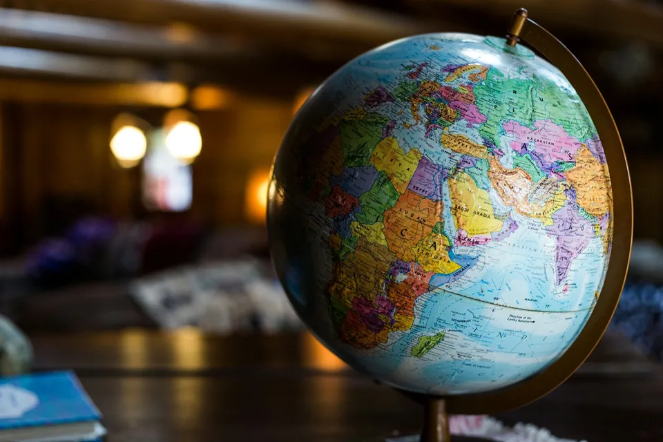 Globo terrestre de mesa em primeiro plano, com um ambiente interno de luz quente desfocado ao fundo.