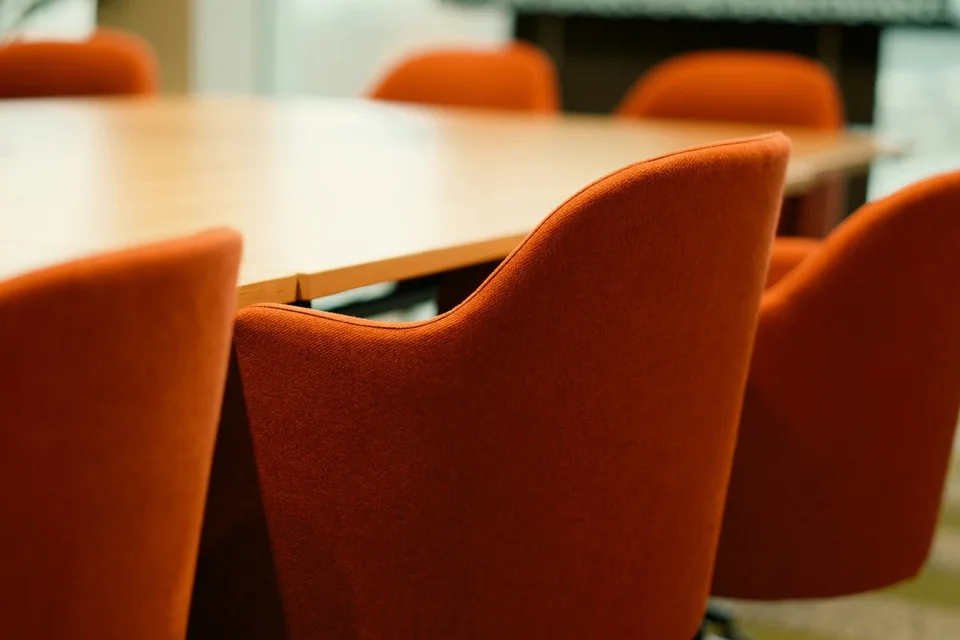 Cadeiras estofadas laranja ao redor de uma mesa de reunião de madeira em um escritório.