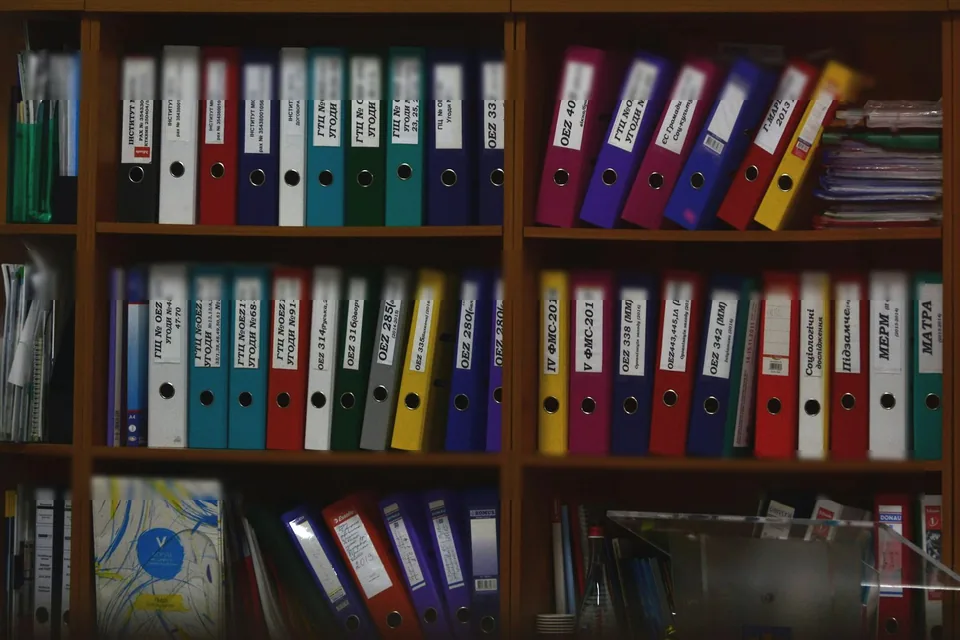 Prateleiras de escritorio com ficharios coloridos enfileirados; rotulos desfocados.