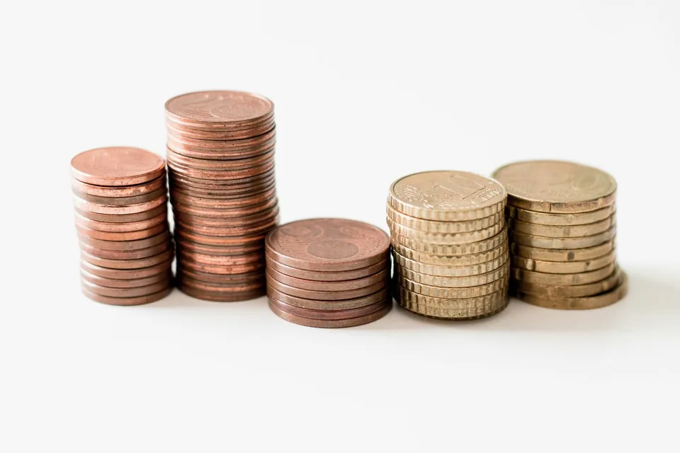 Pilhas de moedas de alturas diferentes, separadas lado a lado sobre uma superfície branca.