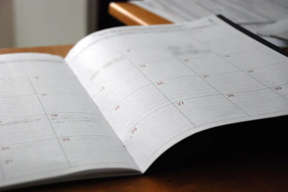 Agenda mensal aberta sobre mesa de madeira, com anotações desfocadas.